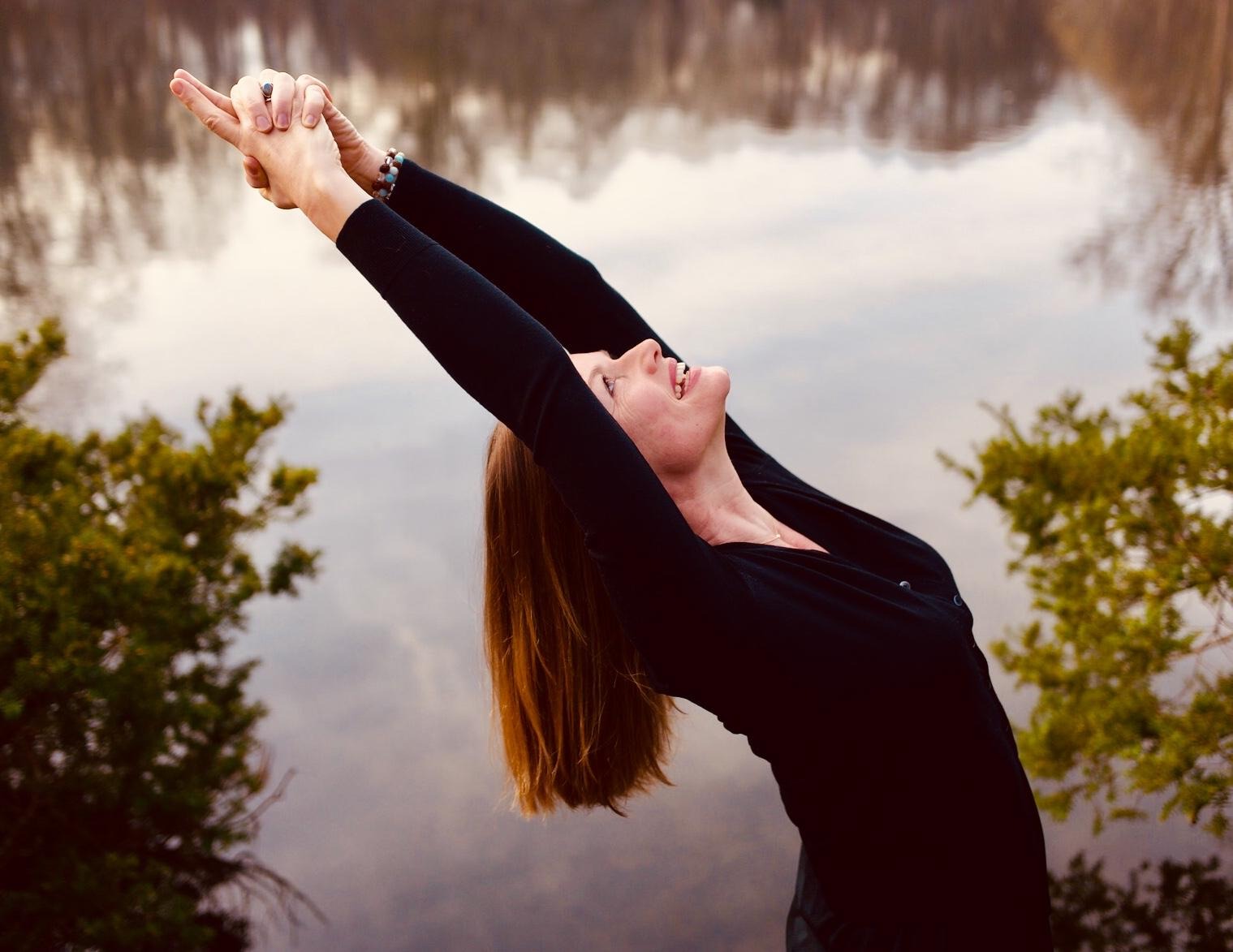 Muriel reaching overhead beside a lake