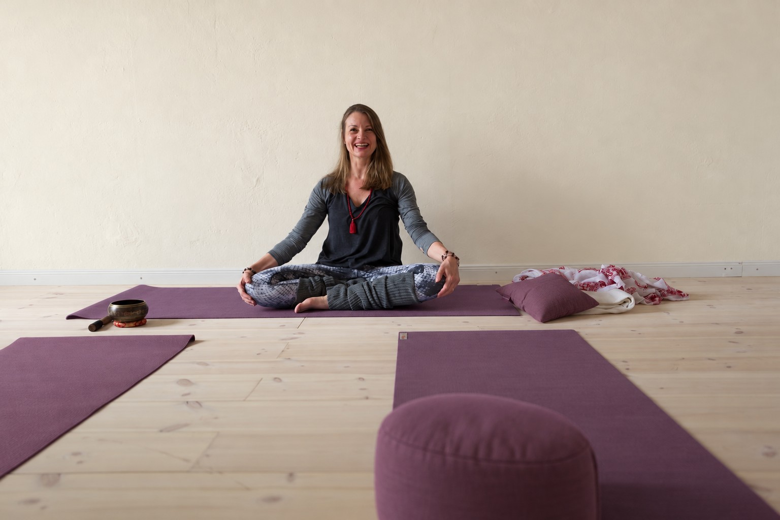 Muriel seated in her practice room with muted purple yoga mats and matching cushions
