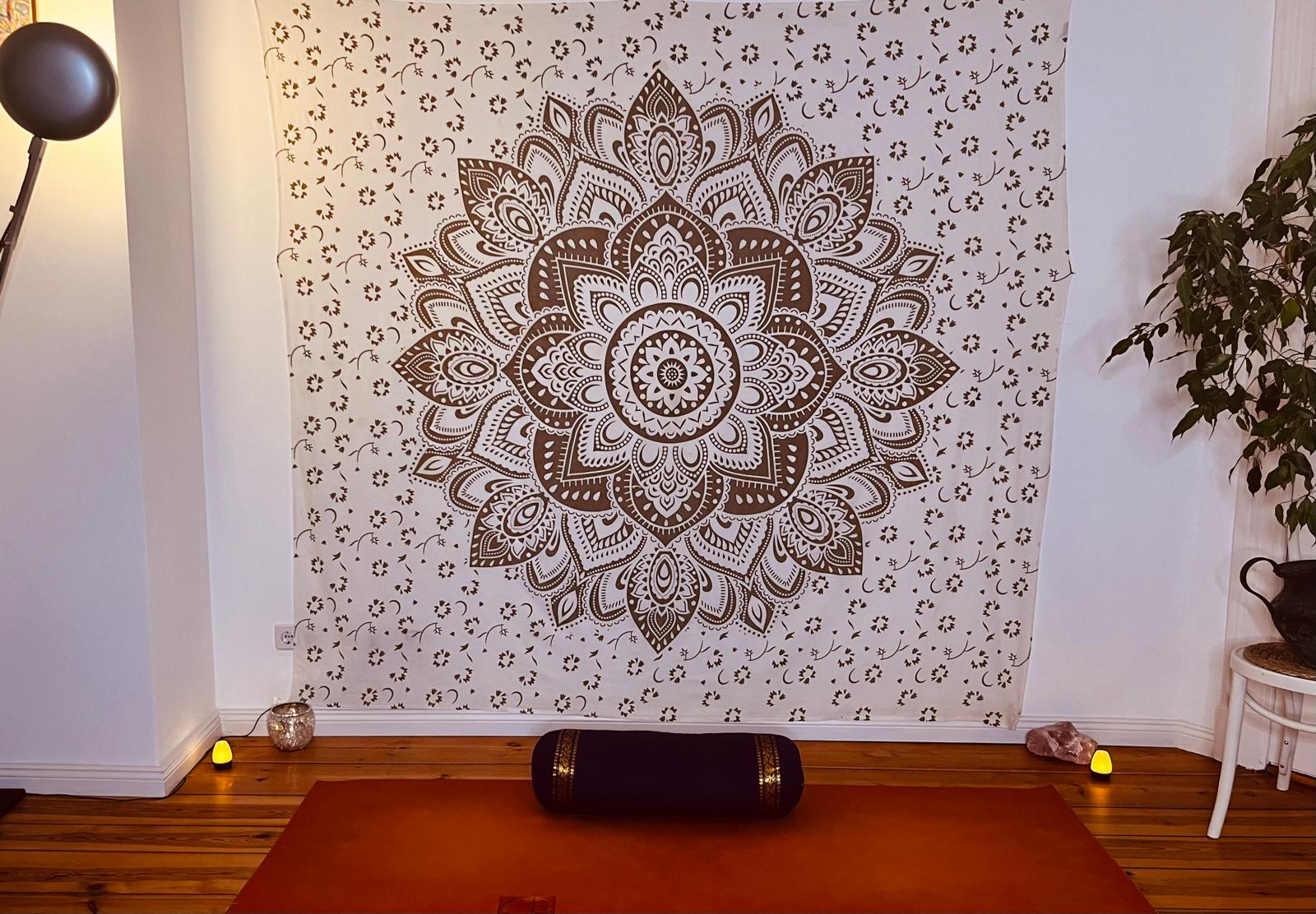 A home yoga space with a mandala wall hanging, orange mat and purple bolster